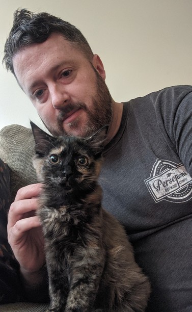 Photo of a guy and a tortoishell kitten on a couch