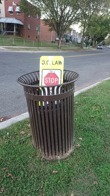 A trash bin. Placed in it is a "stop for pedestrians in crossing" sign that's typically placed in the middle of a crosswalk to calm traffic