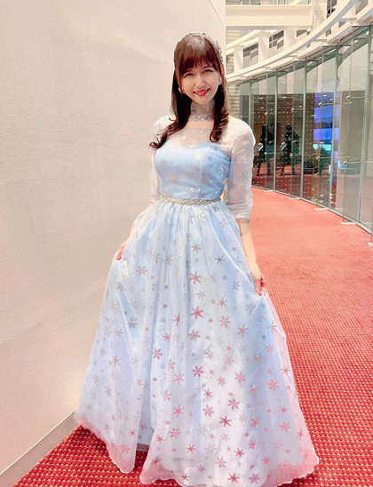 Kikuko wearing a light blue dress with a star pattern, standing in a hallway, smiling.
