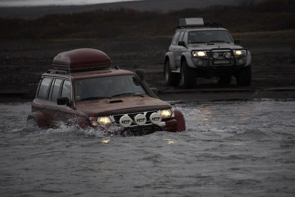 Some 4x4s trek through a river. The water is up to the headlights on one vehicle.