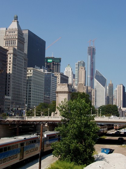against a backdrop of blue sky, Chicago's skyscrapers stand tall. Immediately in front of the viewer, in a cutting, the Metra trains run beside S Michigan Avenue.