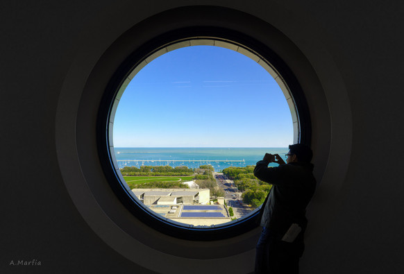 A color photography taken inside the Railway Exchange Building during Open House Chicago 2011. Pictured is a large round window overlooking Grant Park. A man is seen snapping a picture from the right corner.