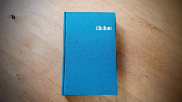 Mein Ausgabe des Schachbuches: Ein einfaches Buch in textilem Einband in dunklem Türkis, auf dem schlicht "Schachbuch" in der rechten oberen Ecke steht.