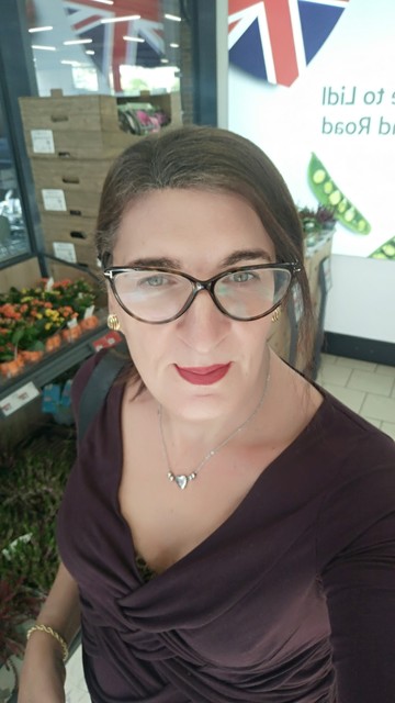 A selfie of a brunette trans woman in a wine colored top  with a Lidl sign in the background