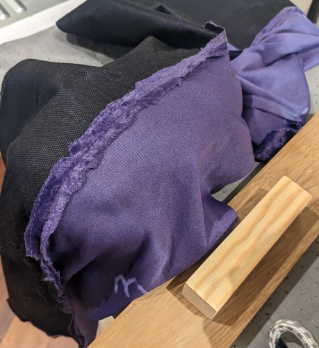 A wooden board with a handle lies next to a purple piece of fabric, joined to another piece of fabric, interfaced in black. Clearly this is a garment of some detailed construction. 

The curve of the seamed pieces of fabric is supported by something underneath, not visible except for the way it lets the curved seam drape open
