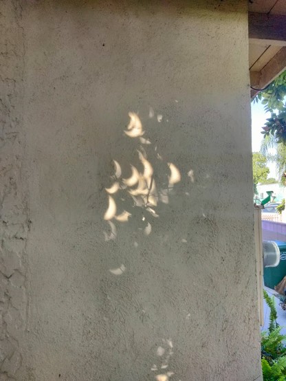 Crescent shapes projected on a mostly shaded wall, during partial eclipse.