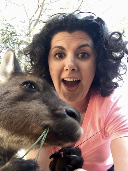 Selfie of the poster smiling widely and a tiny kangaroo munching on a blade of grass in the front of the frame.