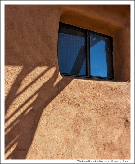 A window inset in an adobe wall (actually plastered straw bale construction), with the shadow of a ladder