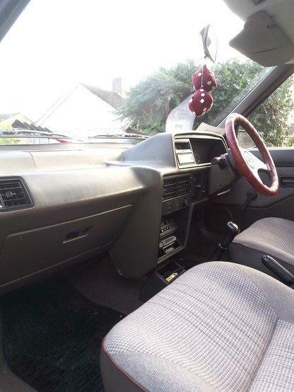 The interior of a 1988 Austin Maestro in Flint trim with tweed seats trimming in claret piping.  There are several 1990s period accessories  colour coded to match the interior.