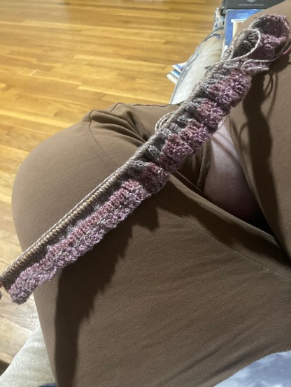 Purple and grey yarn on a knitting needle, forming the rob of a sweater