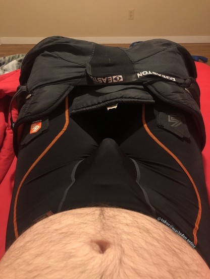Held my camera pointing at my torso facing my crotch. My hairy belly is exposed and my black hockey pants are down to my knees, exposing my black compression shorts with a cup inside.