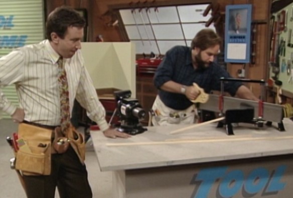 Im Set der Heimwerker-Sendung „Tool Time“. Tim stützt sich sauer schauend am Tisch ab. Neben ihm sägt Al gerade eine Holzleiste auf Gehrung.