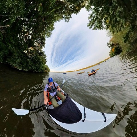 Photo of several people kayaking on a lake, with green trees lining the shoreline.