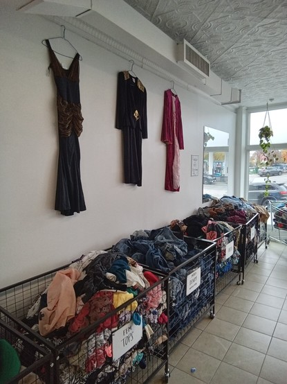 three long dresses hanging on the wall above bins of clothes in a store