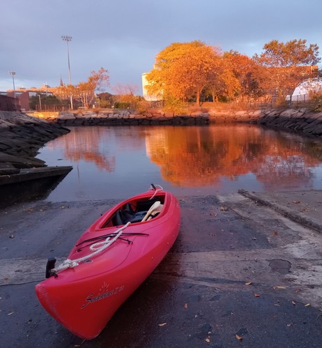Photo of red kayak on boat ramp, in front of trees with yellow leaves.