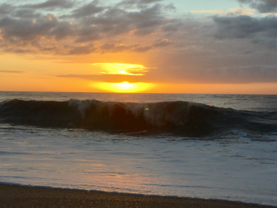 Color image of sunrise as a wave crashes on a placid beach in Coastal Carolina.