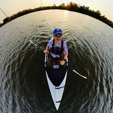 Photo of a person kayaking in the middle of a lake, smiling like a goofball at the camera.