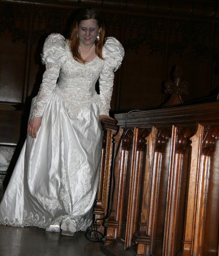 An actor performs a horror comedy parody walking through the pews of a university chapel portraying a zombie in a large white wedding dress.