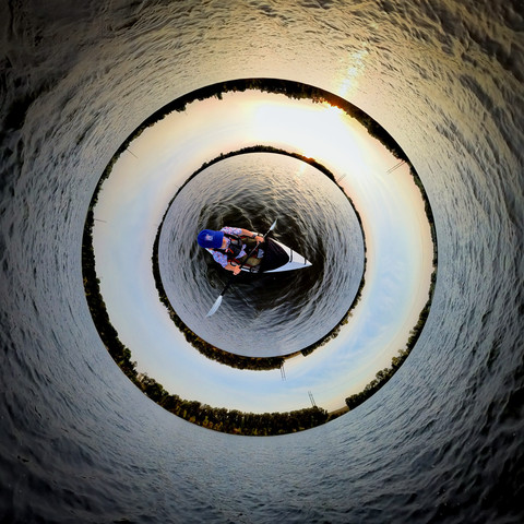 Photo of a person kayaking on a lake. The image combines two "tiny planet" into a single unnatural view of the scene.
