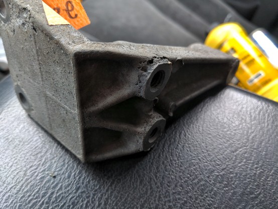 A used aluminum bracket showing serious signs of decay. The metal is flaking away and almost porous. The damage is consistent with acid damage (likely murietic acid used to remove oil and grease). Small bits of metal are actually flaking off onto the surface the bracket is resting on.
