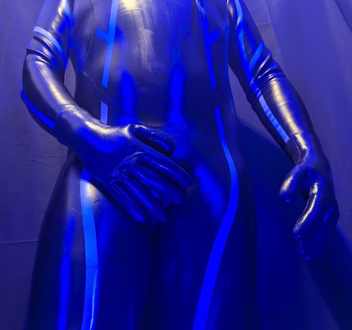 Wearing a shiny Blue70 wetsuit, neoprene gloves and neoprene hood. Holding hand over crotch