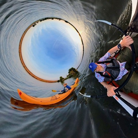 Photo of two people kayaking on a deep blue lake under light blue skies filled with wispy white clouds.