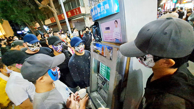 Eight people clad in black with “Eight Generals” face painting surround a person dressed as an ATM during the Halloween Parade in Hsinchu City on Saturday.