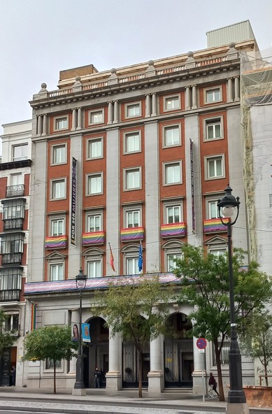 7stÃ¶ckiges GebÃ¤ude mit drei TorbÃ¶gen im Erdgeschoss. Quer Ã¼ber das erste Stockwerk der Fassade ist eine Trans-Fahne ,(blau-rosa-weiÃŸ-rosa-blau) angebracht. Im Stockwerk darÃ¼ber an den 5 Fenstern Regenbogen-Fahnen.