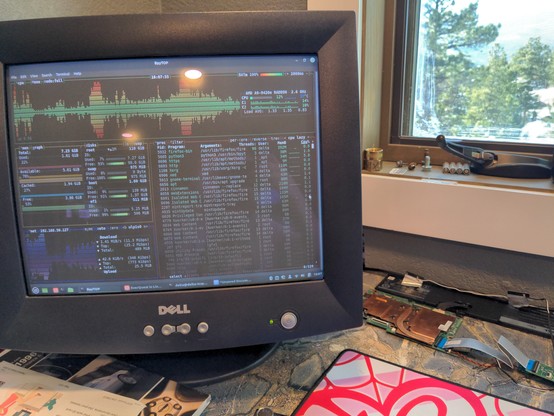 An old CRT monitor from Dell, showing the output from pytop (a command line based resource monitoring tool). The computer is running Linux Mint, with the task bar visible. The computer itself is a loose pile of circuit boards and cables, sitting on a tile desk surface (nonconductive).