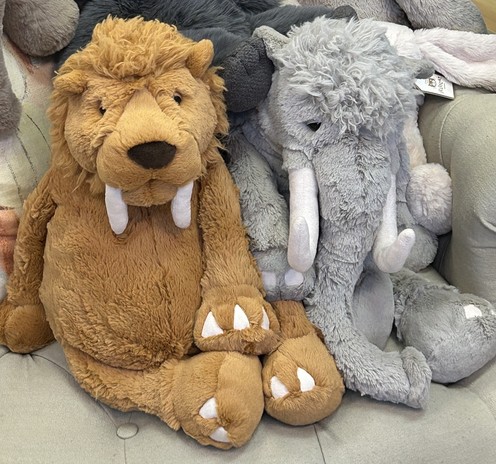 Brown saber toothed tiger stuffed animal (maybe) next to his friend a grey mastodon stuffed animal (maybe).