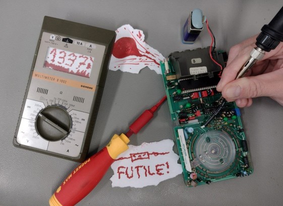 Zerlegte Multimeter-Komponenten eines Siemens B1002 auf einem Labortisch. Das Display des Oberteils zeigt gemalt blutunterlegt den Schriftzug "1337".
Eine Botschaft liegt dabei, ein Widerstands-Symbol, darunter der blutrote Schriftzug "FUTILE!"
Unter der Platine eine gemalte Blutlache. Ein Schraubendreher "steckt" darin.
Eine Hand hält einen Lötkolben.
An der Spitze.
Das Grauen. Das Grauen...