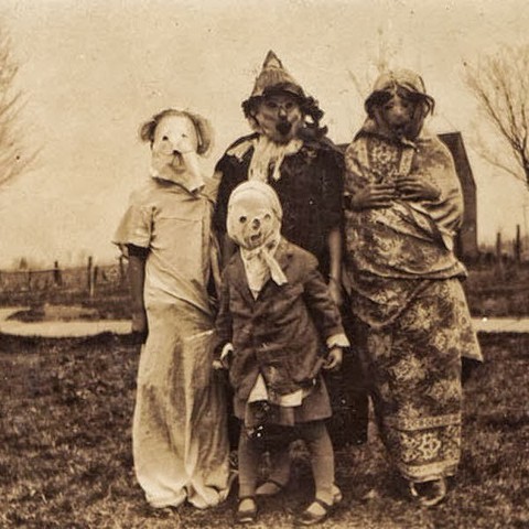 A set of vintage black & white photos of children wearing homemade Halloween costumes. They are very disturbing images, to put it mildly. 

Four kids wearing combinations of dirty clothes, sheets, and blankets have whole-head masks on that may be made out of cloth (but it's hard to tell for sure). Regardless, the cut-out eyes, crooked mouths, and weird wigs and hats make the children appear ghoulish.