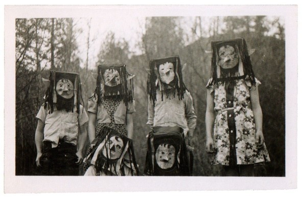 A set of vintage black & white photos of children wearing homemade Halloween costumes. They are very disturbing images, to put it mildly. 

Six kids (?) wearing normal-looking street clothes (pants, shirts, or dresses) but each is wearing a "mask" over their heads. Each "mask" is different. They appear to be made out of boxes that are just big enough to put their heads into. Each one is, of course, flat on the sides and on the top but they're covered in black "hair" that's probably made from yarn, I'd guess. The "hair" hangs down the sides of each "mask", including the face - except that each face has been cut free of the yarn so that the result is a black head with a white face. (Probably looks pretty spooky in the dark.) Each face has a cone nose (think of having an ice cream cone in the center of your face) with eyes and a mouth cut out of the box so the wearer can see and speak.