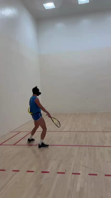 A human dog in blue shirt and shorts trying to chase the ball in a racquetball court.