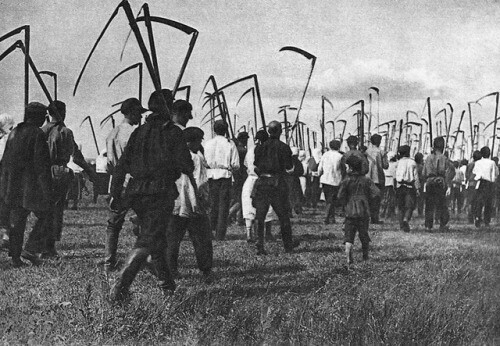 People in a mob marching through a field carrying scythes.