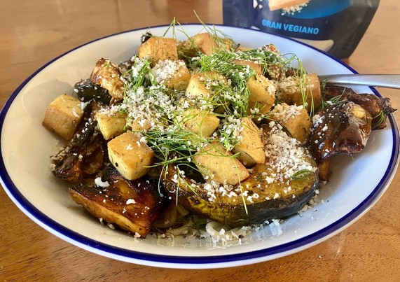 Bowl containing barely visible spaghetti engulfed by various roasted sliced squashes & fennel, golden tofu cubes and a sprinkling of fennel fronds, black pepper and vegan parmesan (the â€˜gran vegianoâ€™ packet is visible behind)