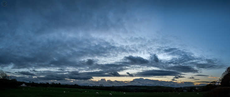 Wide angle shot of dawn/sunrise over Cumbrian hills with farmland in foreground and spectacular clouds above with sun starting to shine through