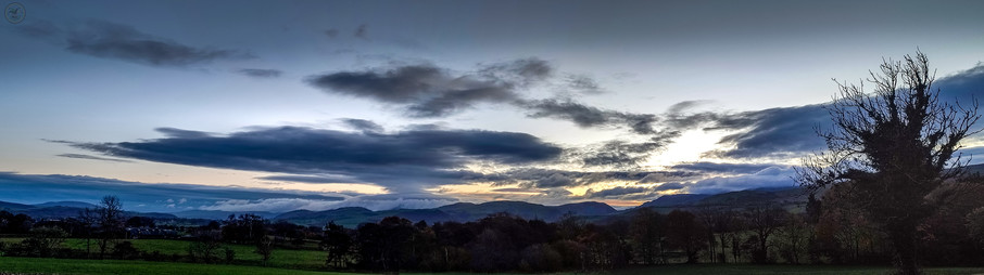 Wide angle shot of dawn/sunrise over Cumbrian hills with farmland in foreground and spectacular clouds above with sun starting to shine through