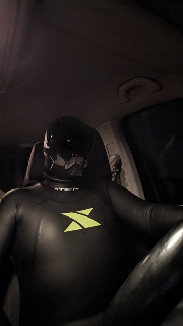 Sitting in driver's seat of a car, wearing a wetsuit, gloves, neoprene hood and cybermask