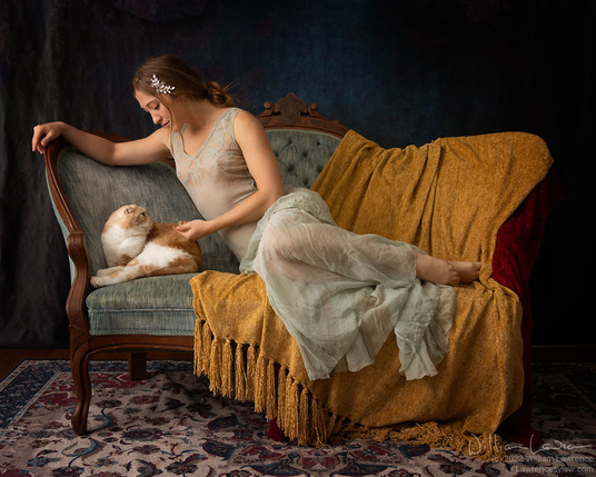 Model Lucy Artmodel reclines on a settee, petting Gus, a cameo tabby Scottish Fold cat.  Lucy is wearing a sheer teal vintage gown.