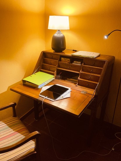 An old writing desk, with a closed file and an iPad, bathed in warm light.