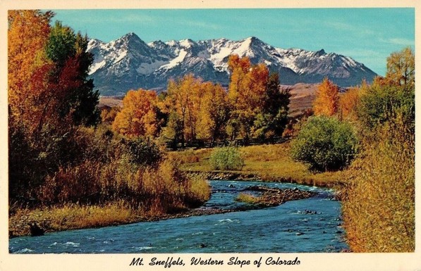beautiful image of a winding river with autumn colored trees on either side and snow capped mountains in the back.