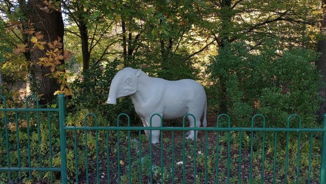 A model of a creature that would look like a small horse, but its legs are too short, it has a short, cylindrical trunk for a nose, rounded ears like a rat, and a bulb-ended tail like a donkey (or, if you prefer, a lion).

It is a uniform grey in colour, and very clean, so it looks like it's been made out of plasticine. It's standing in a small copse or spinney, behind a fence of green railings, and bears a blankly mournful expression.