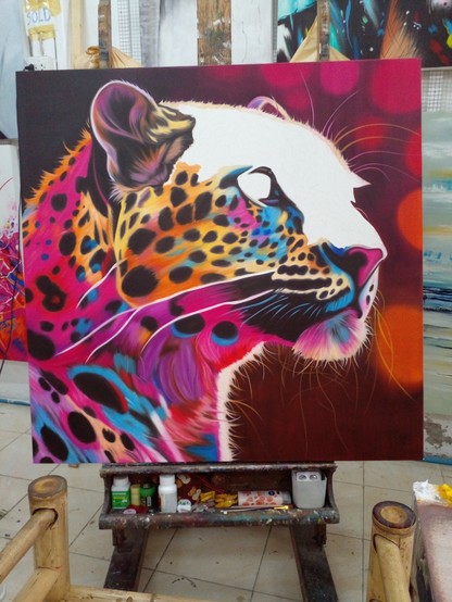 a painting of the head of a leopard, looking to the right, the background is tones of orange and pink, the face of the leopard is a swirling mix of pinks, yellows, purples, blues, and black, the top of the skull and bridge of the cat's nose are still blank, unpainted, the painting is in the process of being painted