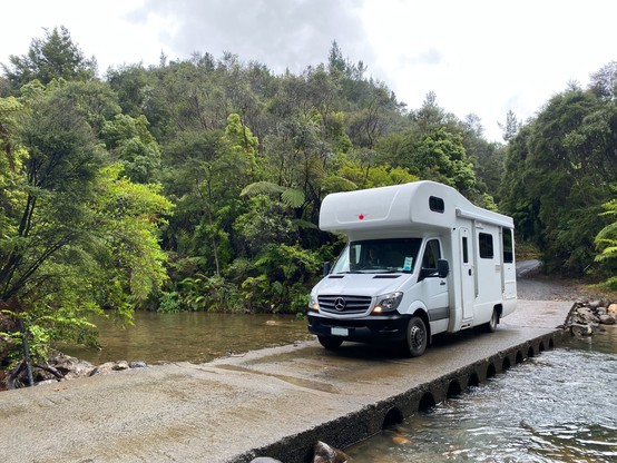 Motorhome crossing a ford, seen from front in overcast weather, with native bush surrounding
