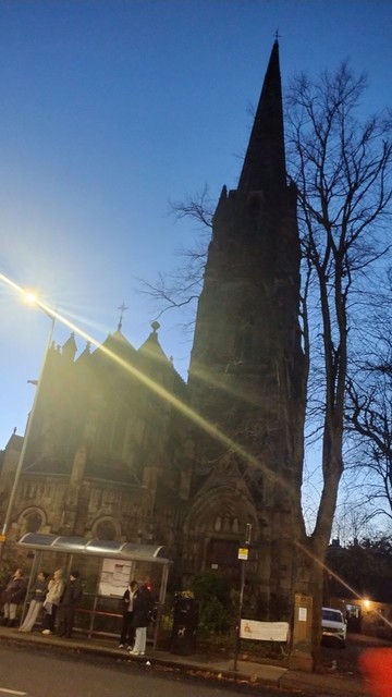 Gothic facade and tall spire of Christ Church semi silhouetted by last, fading blue light of dusk sky behind it