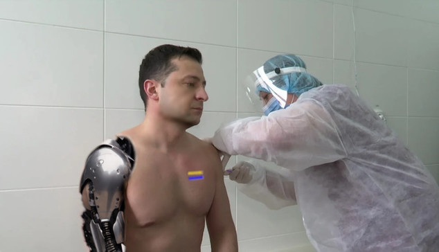 Ukrainian leader Zelenskyy has his right arm desheathed revealing a robotic arm. his shirtless chest has two status lights which are yellow and blue. an engineer in a clean suit is performing maintenance on his left arm out of view of the camera.