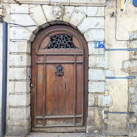 Wooden door with an ornate knocker and a scowling face carved in stone above it.