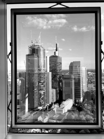 Schwarz-weisses Hochformat. Blick durch ein Fenster eines Hochhauses auf andere Hochhäuser.