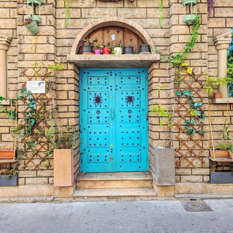 Bright blue door studded with metal. There are flower pots in the ledge of the fanlight.